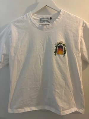 Vit Casablanca t-shirt - Vit t-shirt från Casablanca med färgglatt tryck fram och stort grafiskt tryck på ryggen med texten 'Avenida Casablanca'. Klassisk passform och rund hals. Perfekt för dig som gillar stilrena plagg med unika detaljer.