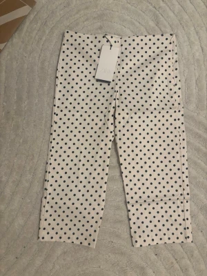 Vita leggings med svarta prickar - Snygga vita leggings med svarta prickar och rak passform. Stretchigt material som sitter bekvämt och ger en cool retrovibe. Perfekta att styla med en oversized hoodie eller crop top för en trendig look.