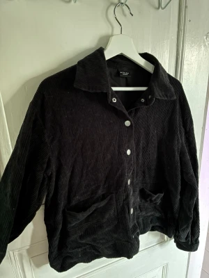 Svart overshirt från Bitte Kai Rand - Snygg svart overshirt i bredspårig manchester från Bitte Kai Rand. Jackan har krage, tryckknappar framtill och två stora fickor. Perfekt lager-på-lager-plagg med avslappnad passform och cool retrovibe.