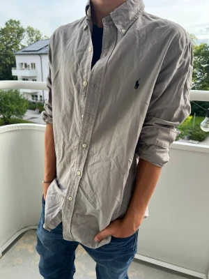 Ralph Lauren grå skjorta - Snygg grå skjorta med klassisk krage och knappar framtill. Skjortan har lång ärm och en logga broderad på bröstet. Storlek S. 