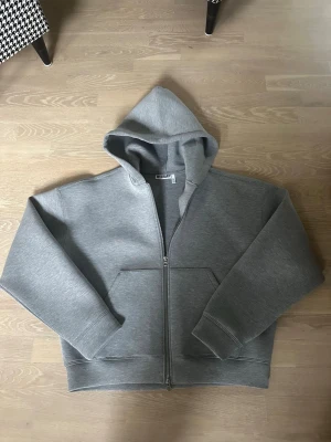 Grå scuba zip hoodie - En stilren grå hoodie med dragkedja framtill och stor huva. Hoodien har två fickor på magen och ribbade muddar vid ärmar och nederkant. Perfekt för dig som gillar streetwear. Skriv om du har frågor😊