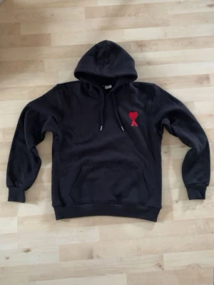 Svart ami Paris hoodie  - En svart ami Paris hoodie med den röda hjärt-loghan fram på bröstet. Är i xl i barnstorlek men är stor i storleken så sitter som en s/m i vuxenstorlek. Jag har köpt den på plick men passade ej mig. 