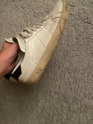 Saint Laurent  låga sneakers med svart detalj - Snygga vita sneakers i läder med klassisk låg profil och vita snören. Skorna har en svart detalj vid hälen och en beige sula med struktur. Perfekta för en clean och stilren look.