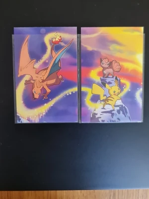Pokémon samlarkort Charizard & Pikachu - Två Pokémon samlarkort med färgstarka motiv av Charizard, Pikachu och Vulpix. Korten har lila och gula bakgrundsfärger och är tillverkade i glansigt papper. Perfekt för dig som gillar Pokémon och vill utöka din samling.
