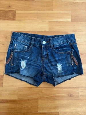 Mörkblå jeansshorts med dragkedjor - Står storlek m men passar xs/s och ca w24/25🥰🥰Snygga mörkblå jeansshorts med slitna detaljer och rå kant. Shortsen har dragkedjor med läderdetaljer framtill och klassiska fickor både fram och bak. Perfekta för sommaren och ger en avslappnad streetstyle-vibe.