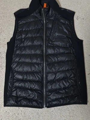 Svart dunväst från Parajumpers L - Snygg svart dunväst från Parajumpers i storlek L. Västen har quiltad design, dragkedja framtill, bröstficka med dragkedja och två sidofickor. Insidan har orange detaljer och etiketten 'WARM UP'. Perfekt för lager på lager och streetwear.