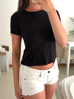Svart croppad t-shirt - En enkel svart croppad t-shirt med rund hals och korta ärmar. T-shirten har en rak passform och är tillverkad i mjuk bomull, perfekt för en avslappnad och trendig look.