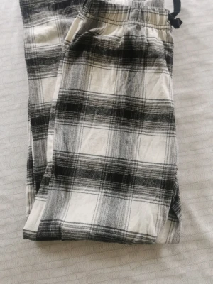 Rutiga pyjamasbyxor från H&M - Säljer ett par svartvita rutiga pyjamasbyxor från H&M i storlek 146/152. Byxorna har resår i midjan och snörning för extra komfort. Tillverkade i mjukt bomullstyg, perfekta för mysiga kvällar hemma.