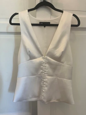 Vit topp från Zara - Stilren vit linnetopp i satin med djup v-ringning och breda axelband. Toppen har en figurnära passform och markerad midja som ger en snygg siluett. Perfekt att styla med jeans eller kjol för en trendig look.