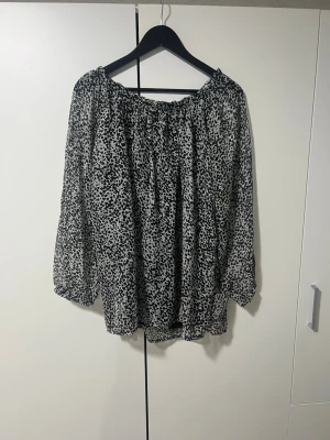 Svartvit offshoulder-blus med mönster - Säljer en luftig svartvit blus med offshoulder-modell och abstrakt prickigt mönster. Blusen har vida trekvartsärmar och resår vid halsringningen. Perfekt till jeans eller kjol för en trendig look.