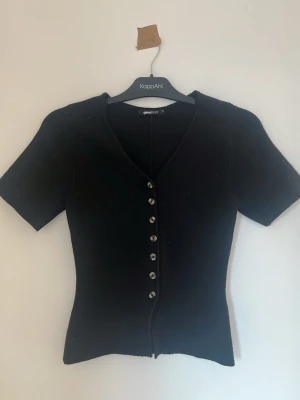 Svart v-ringad topp från Gina Tricot - Svart topp från Gina Tricot med v-ringning och korta ärmar i storlek XS.