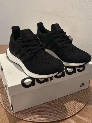 Adidas Ultraboost - Snygga svarta Adidas Ultraboost sneakers med stickad ovandel i mesh för bra andningsförmåga. Skorna har vita Boost-sulor för extra komfort och svarta detaljer i plast runt snörningen. Perfekta för dig som gillar stilrena och bekväma sneakers.