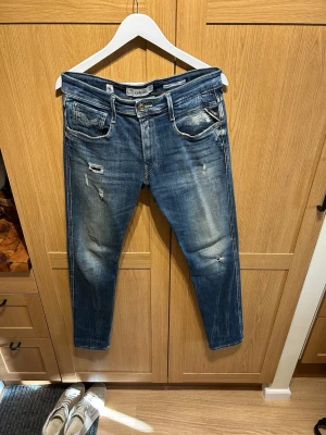 Replay Anbass - Säljer ett par blå slim fit jeans från Replay, modell Anbass. Jeansen har slitningar och en tvättad look med detaljerade slitna partier och fem fickor. Bara att skriva vid frågor Storlek 32