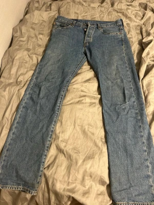 Blå Levis 501:or jeans  - Klassiska blå jeans med rak passform och fem fickor. Jeansen har normal midja, knappgylf och subtila slitningar framtill. Tillverkade i slitstark denim med kontrastsömmar och patch bak i midjan. Pris kan diskuteras