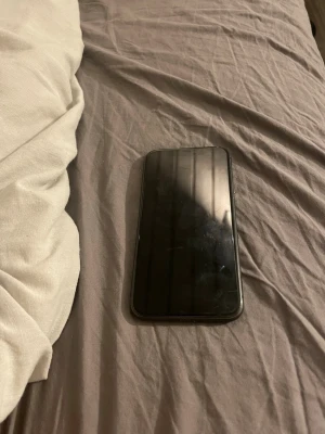 Svart iPhone 11 - Säljer en svart iPhone med stilren design och rundade kanter. Baksidan är i glas och mobilen har två kameror på baksidan samt Apple-loggan i mitten. Perfekt för dig som gillar snygg och modern teknik.