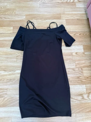 Svart offshoulder klänning S - Snygg svart offshoulder klänning med smala axelband och kort ärm. Klänningen har en kroppsnära passform och är knälång, perfekt för dig som gillar en stilren och enkel look. Lite för tajt 