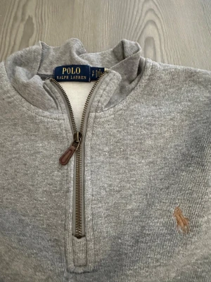 Grå halvzip från Polo Ralph Lauren - Klassisk grå tröja med halv dragkedja från Polo Ralph Lauren.  Storlek S