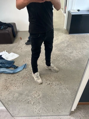 Svarta nudie jeans - Modellen på bilden är 180cm lång och väger ca 62kg. Säljer ett par svarta slim fit jeans med klassisk femficksdesign och smal passform. Jeansen har normal midja och är tillverkade i ett stretchigt material som sitter snyggt längs benen. Perfekta för en clean och stilren look.