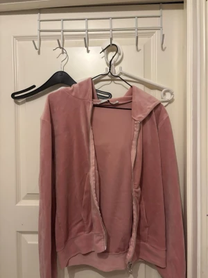 Rosa hoodie med dragkedja  - Mysig rosa hoodie i mjuk velour med huva och dragkedja framtill. Hoodien har långa ärmar och två fickor på sidorna. 