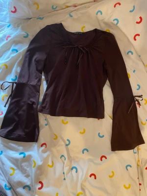 Brun långärmad topp med knyt från SHEIN - Snygg brun långärmad topp från SHEIN med utsvängda ärmar och dekorativa knytband både vid halsringningen och på ärmarna. Perfekt för dig som gillar trendiga detaljer och en mjuk, bekväm känsla.
