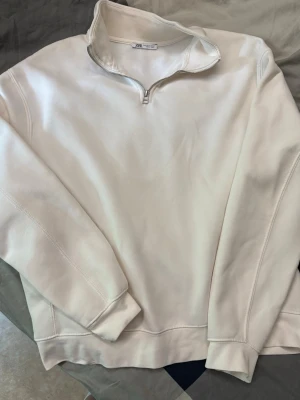 Vit halfzip hoodie från Zara - Säljer en stilren vit hoodie från Zara med halfzip-dragkedja och hög krage. Tröjan har långa ärmar och ribbade muddar. Perfekt för dig som gillar en clean och enkel look. Materialet känns mjukt och bekvämt.