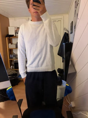 Vit stickad tröja med rund hals - Säljer en enkel och stilren vit stickad tröja med rund hals och ribbade muddar vid ärmslut och nederkant. Perfekt att slänga på sig när det är lite kyligare ute. Passar till det mesta och är lätt att matcha.