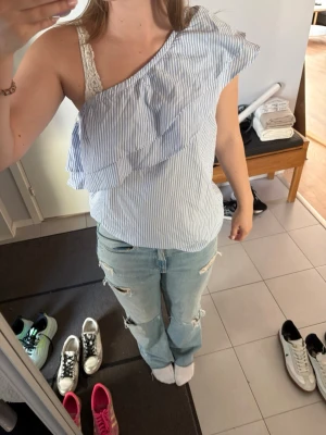 Randig oneshoulder topp med volang - Snygg blå- och vitrandig oneshoulder topp med volangdetalj över axeln. Ganska stor i storleken så skulle säga att den passar M-L. Aldrig använd pga för stor💞