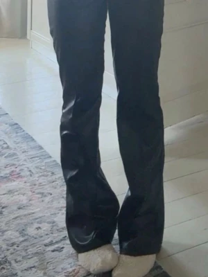 Svarta läderbyxor från Gina tricot - Säljer ett par svarta  läderbyxor  med utsvängda ben och låg midja. Byxorna har en dragkedja framtill och är i mycket gott skick. Snyggt och trendigt plagg som passar perfekt till en cool outfit.❣️de är i storlek 158 men passar mig som har xs