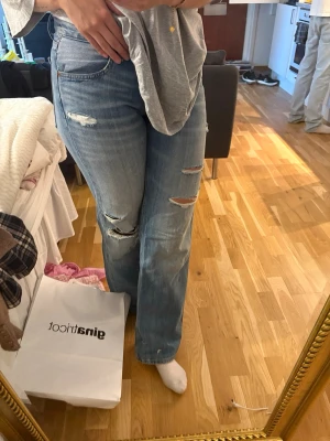 Ljusblå slitna raka jeans - Säljer ett par ljusblå jeans med raka ben och flera slitningar och hål på framsidan. Jeansen har klassisk femficksmodell och är tillverkade i denim. Endast testade, använder ej.
