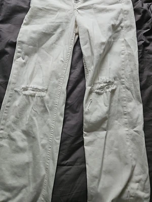 Vita raka jeans med slitningar från KappAhl  - Säljer ett par vita jeans med raka ben och slitna detaljer över knäna. Jeansen har klassisk femficksdesign och är tillverkade i ett kraftigare denimtyg. Perfekta för en avslappnad och trendig look. Storlek 152