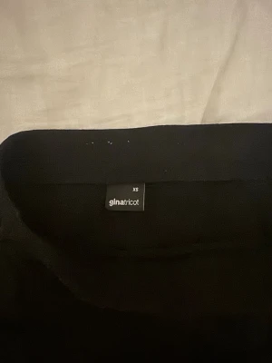 Svart långkjol från Gina Tricot - En svart långkjol från Gina Tricot i enkel och stilren design. Kjolen har rak passform och är gjord i ett mjukt material som känns bekvämt mot huden. Perfekt att matcha med en crop top eller stickad tröja.