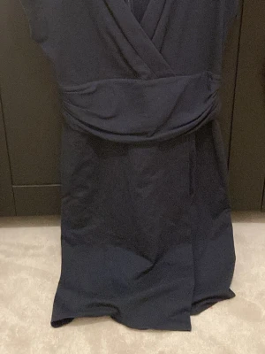 Mörkblå omlottklänning Armani - Snygg mörkblå omlottklänning från Armani Collezioni. Klänningen har en markerad midja och mjukt fallande kjol. Tillverkad i Italien och har en elegant, tidlös design som passar perfekt till många olika tillfällen.