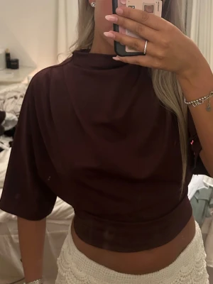 vinröd croppad topp med kort ärm - Säljer en vinröd croppad topp med korta ärmar och hög hals. Toppen har en loose passform upptill och sitter tightare i midjan. Perfekt att styla med höga byxor eller kjol för en trendig look.
