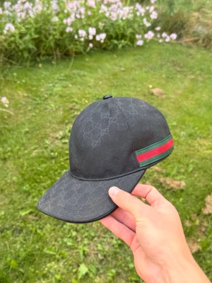 Svart keps GG - Snygg svart keps från GG med klassiskt GG-monogram över hela kepsen och en grön-röd rand på sidan. Kepsen har böjd skärm och justerbar rem bak. Materialet känns slitstarkt och exklusivt, perfekt för dig som vill ha en stilren och lyxig accessoar. Skick 7,5/10✅ Och pris kan diskuteras. Storlek M!!!