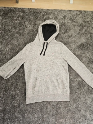 Ljusgrå hoodie från Hollister - Säljer en ljusgrå hoodie från Hollister med svart huva och svarta snören. Storlek M. 