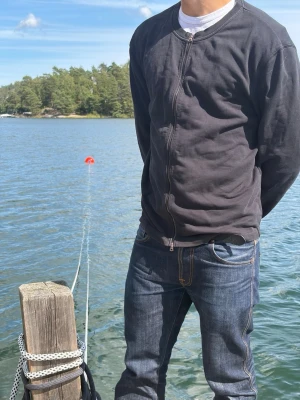 Acne Studios Svart zip cardigan med rund hals - Vintage Acne studio-tillverkas inte längre och svår och få tag i. En enkel och stilren svart cardiganjacka med dragkedja framtill och rund hals. Jackan har långa ärmar och ribbade muddar vid ärmslut och nederkant. Perfekt att slänga på sig över en t-shirt för en avslappnad look.