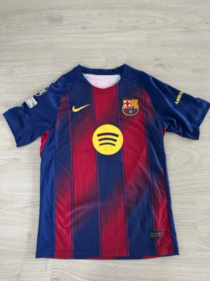 Barcelona matchtröja Nike blå/röd - Säljer en FC Barcelona matchtröja från Nike i blått och rött med gula detaljer. Tröjan har klubbmärke, Nike-logga och Spotify som sponsor framtill. Tillverkad i lätt och ventilerande material, perfekt för fotboll eller träning.