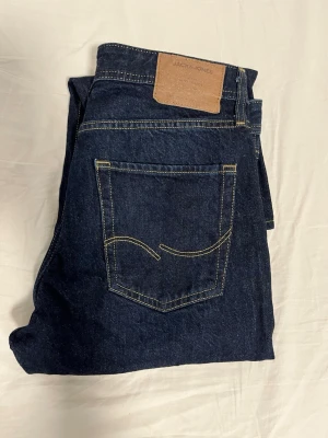 Jack & Jones jeans - Snygga mörkblå jeans från Jack & Jones med relaxed fit. Jeansen har kontrastsömmar i gult och en läderpatch med logga bak i midjan. Tillverkade i slitstarkt denimtyg som passar perfekt till en avslappnad stil. Använt varsamt och inga skador osv.
