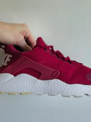 Nike Air Huarache  - Snygga vinröda sneakers med vit, strukturerad sula och matchande vinröda skosnören. Ovandelen är i mesh-tyg för bra andningsförmåga och skon har detaljer i plast längs sidorna. Perfekt för dig som vill ha en sportig och trendig look.
