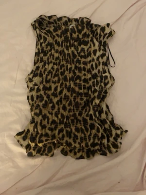 Leopardmönstrad ärmlös topp H&M XS - Säljer en leopardmönstrad ärmlös topp från H&M i storlek XS. Toppen har volangkant upptill och nedtill samt smockad struktur som ger en snygg passform. Perfekt för dig som vill sticka ut med ett djurmönster!