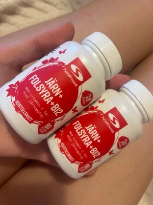 Järn+ Folsyra+B12 kosttillskott - Två vita burkar Healthwell Järn+ Folsyra+B12 kosttillskott med röda etiketter. Innehåller även vitamin C och är märkta med 90 tabletter per burk. Perfekt för dig som vill boosta ditt järnintag.
