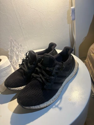 Adidas ultra boost - Snygga svarta sneakers med stickad ovandel och klassiska svarta snören. Skorna har en vit, dämpad sula med textur och svarta detaljer på sidan. Perfekta för dig som gillar sportig och stilren look.