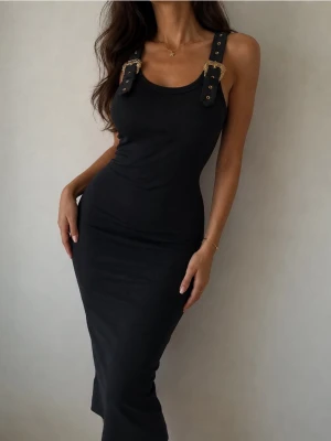 Svart långklänning från Versace Jeans Couture - Versace Jeans Couture klänning – Ny med tagg Elegant svart klänning från Versace Jeans Couture i ribbad stretchkvalitet med exklusiva guldfärgade detaljer och ikoniska spännen vid axlarna. En tidlös modell som passar lika bra till fest som till en mer uppklädd vardagslook. ✔ Ny med originaltagg kvar ✔ Exklusiva Versace-detaljer ✔ Figurnära och smickrande passform ✔ Stretchigt och bekvämt material ✔ Klassisk svart färg som aldrig går ur stil Klänningen är oanvänd och i nyskick. FRAKTAR INOM 24H🩷