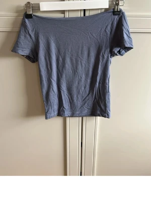 Ljusblå topp - Säljer en ljusblå topp med korta ärmar. Toppen har en enkel och stilren design i mjukt bomullsmaterial och sitter snyggt tight mot kroppen. Perfekt till jeans eller kjol för en trendig look.