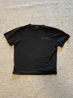 Svart t-shirt från MM Sports - En stilren svart t-shirt från MM Sports med diskret logga på bröstet. Klassisk passform och rund halsringning, perfekt för en sportig och avslappnad look. Tillverkad i mjukt bomullsmaterial.