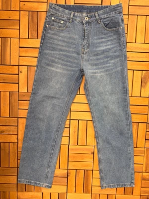 Grå raka jeans med fem fickor - Säljer ett par klassiska grå jeans med rak passform och fem fickor. Jeansen har ljusa slitningar framtill och normal midja. Tillverkade i denim med synliga sömmar och bälteshällor. Perfekta för en avslappnad och stilren look.