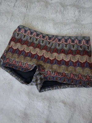 Broderade shorts med vågmönster - Unika shorts med broderat vågmönster i flera färger som beige, röd, blå och grön. De har en tight passform och är tillverkade i ett tjockare tyg med broderade detaljer. Perfekta för dig som vill sticka ut med ett färgglatt plagg.
