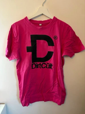 Rosa DirtCult t-shirt  - Snygg rosa t-shirt från DirtCult med stort svart tryck och logga på bröstet. Klassisk rund hals och korta ärmar. Den är stor i storleken. 