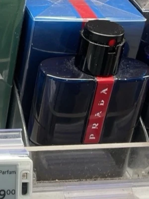 Prada marinblå parfymflaska - Snygg parfym från Prada i en marinblå, glansig flaska med en röd vertikal rand och tydlig logga. Flaskan har en rund, svart kork med en röd detalj på toppen. Kommer i matchande blå förpackning med röd rand.