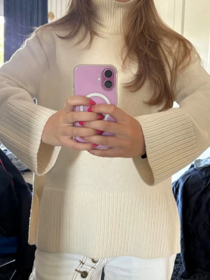 Krämvit polotröja med vida ärmar - Aldrig använd med lappen kvar!Säljer en krämvit stickad polotröja med bred ribbstickning vid hals, ärmslut och nederkant. Tröjan har en avslappnad passform och vida ärmar. Perfekt för lager på lager och riktigt mysig till hösten.
